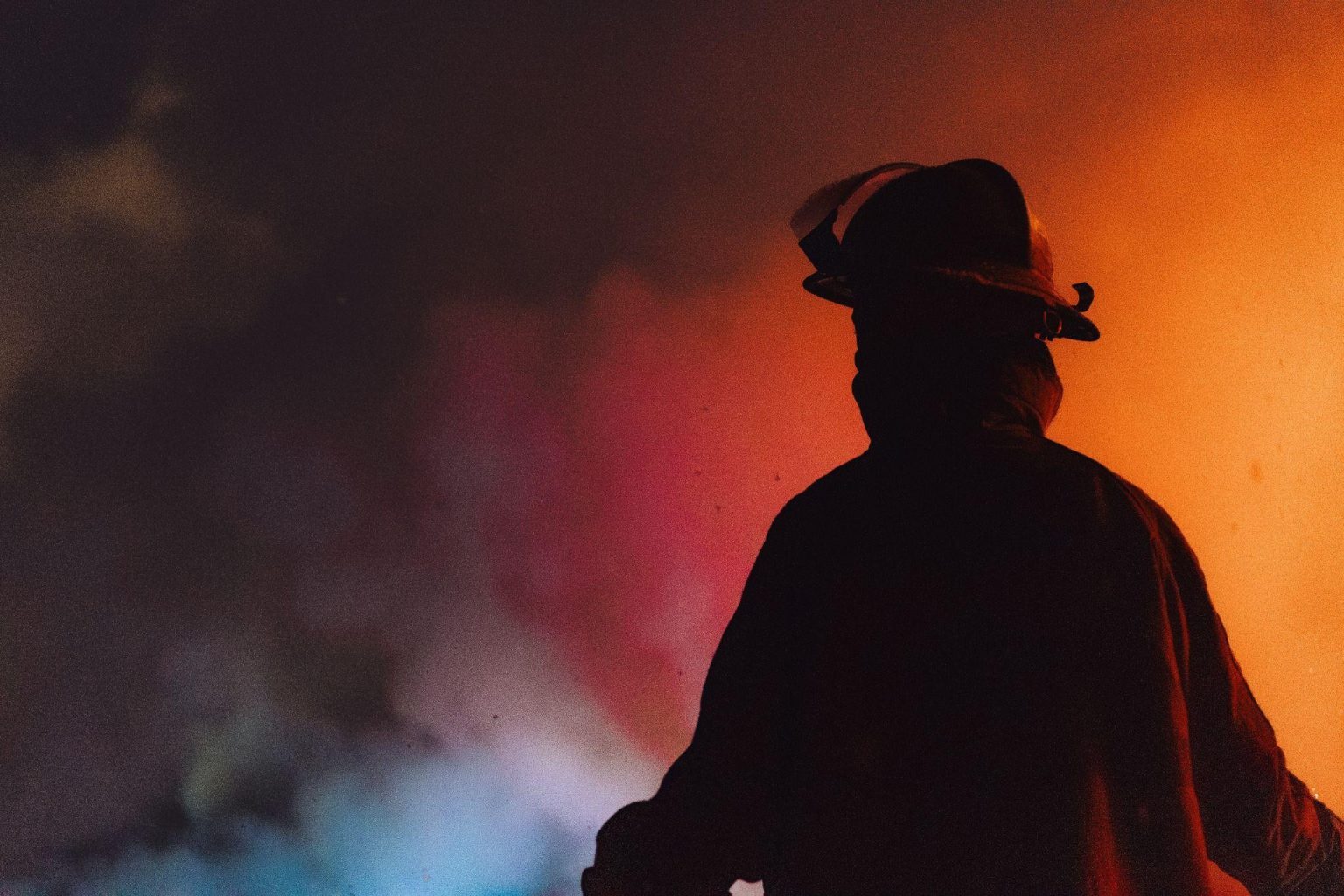 Silhouette of a firefighter against the smoke and glow of a distant fire