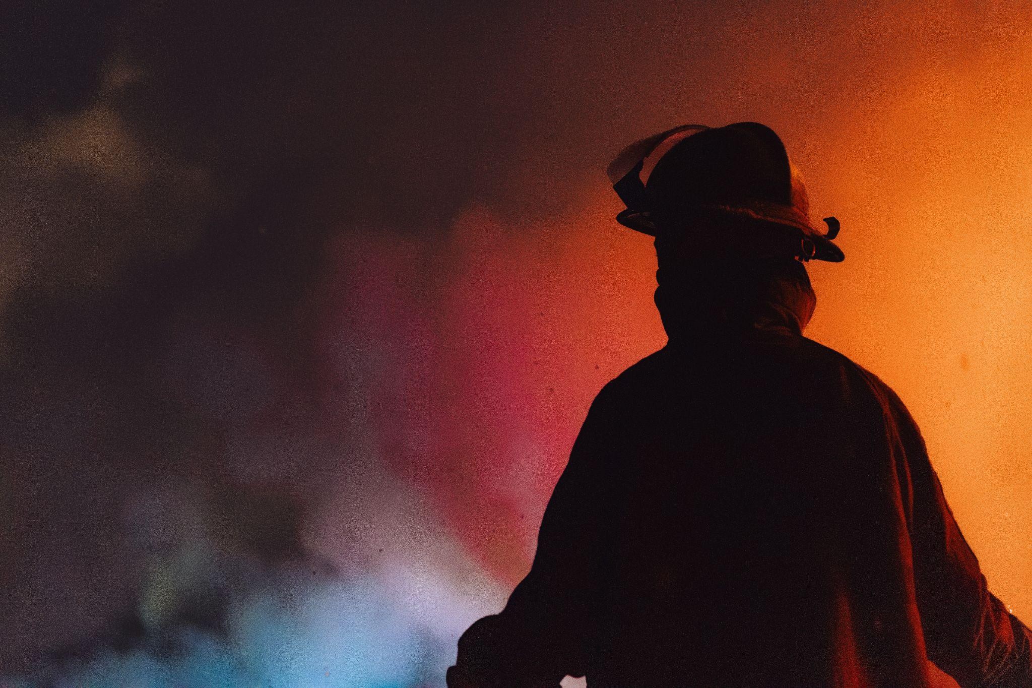 Silhouette of a firefighter against the smoke and glow of a distant fire